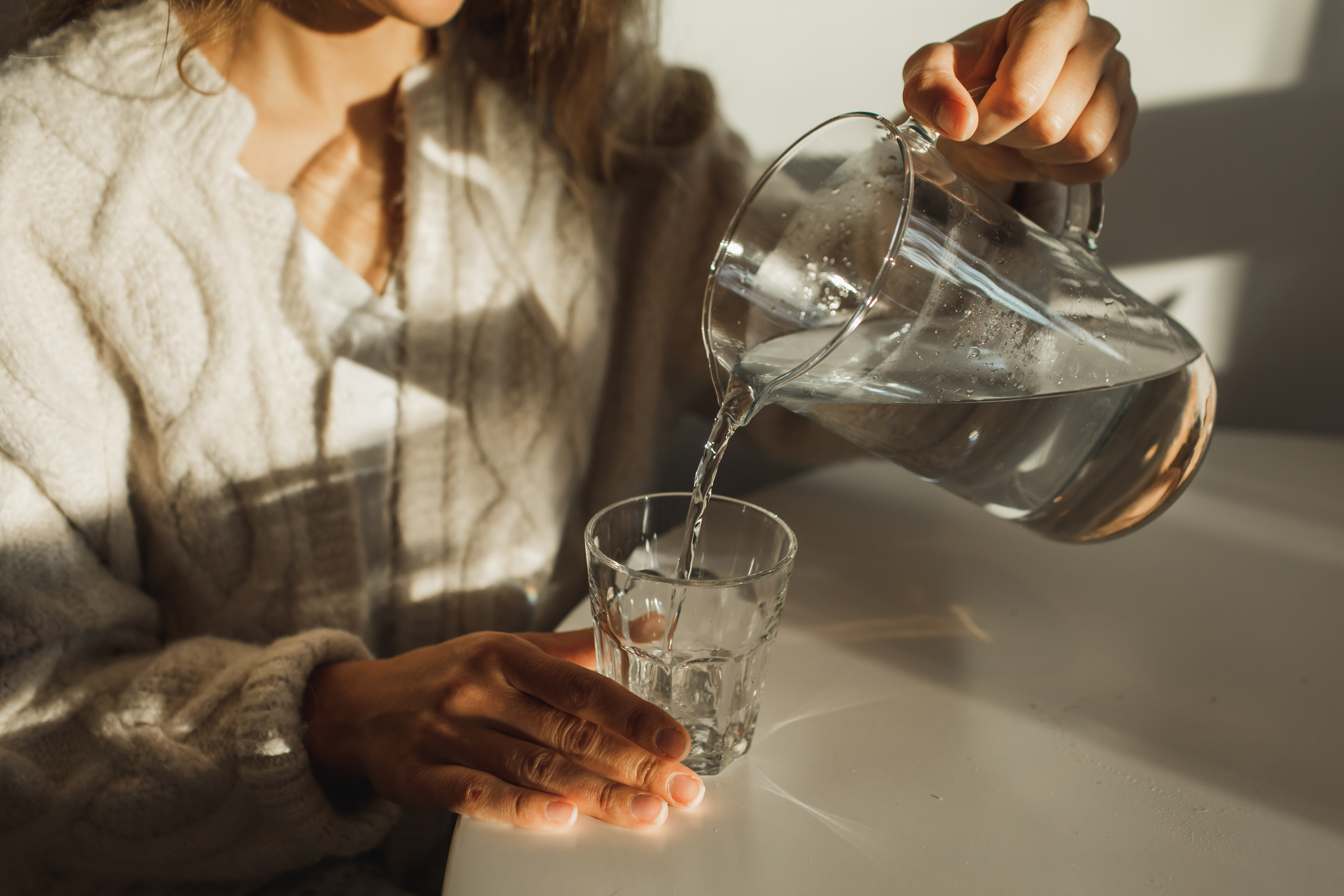 Frau schenkt sich ein Glas Wasser ein