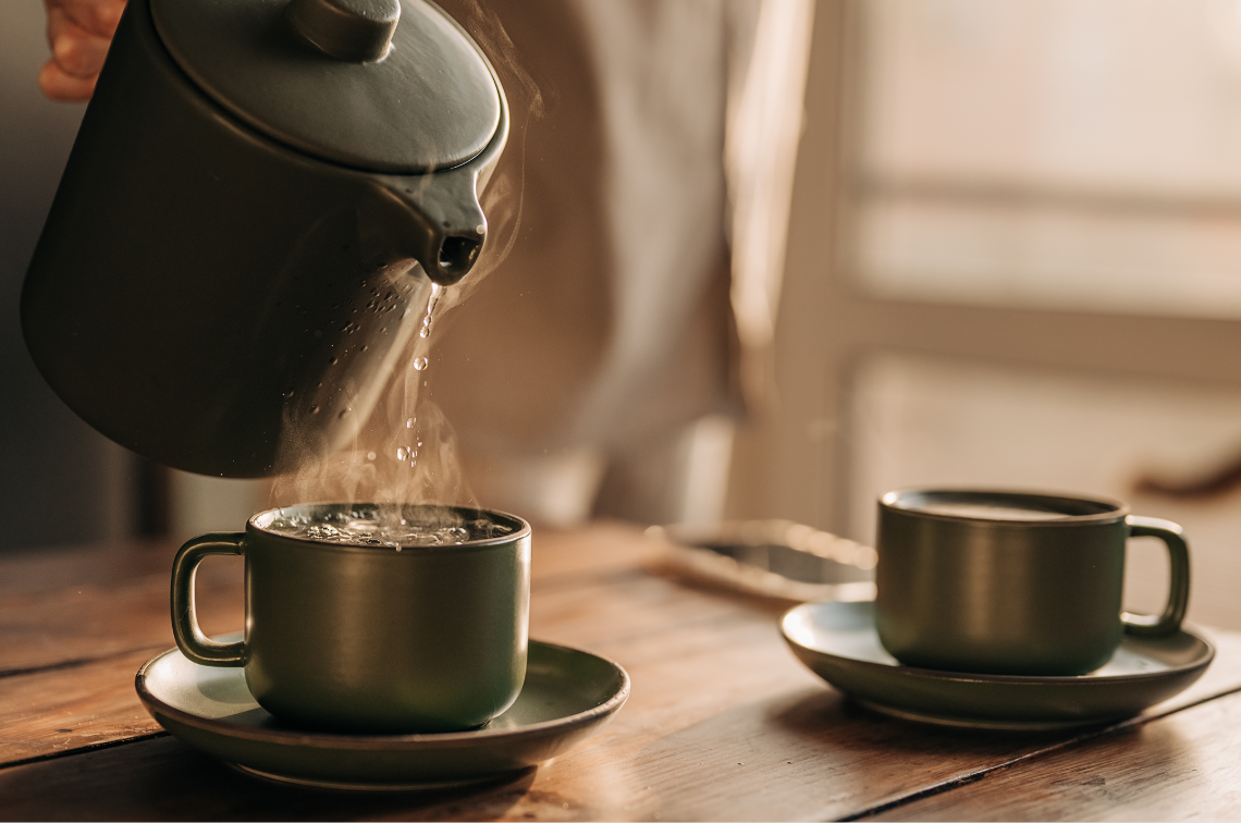 Frischer Tee wird aus einer Teekanne in eine Tasse geschenkt